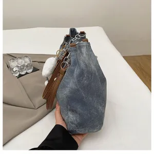 Denim shoulder bag side detail featuring chain straps and cute fluffy white plush pendant.