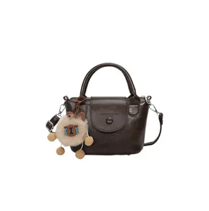 Retro brown leather mini top handle handbag with plush charm for women daily commuting style.