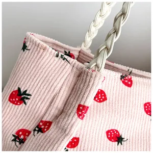 Vue détaillée du sac cabas en velours côtelé rose avec motif de fraises et anses tressées en cuir.