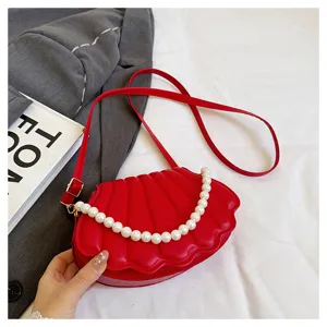 Red shell-shaped crossbody bag detail, elegant pearl handle, premium PU leather texture.