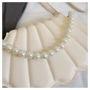 Close-up of cream seashell crossbody bag featuring elegant pearl handle, chic modern design.
