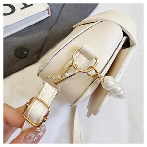White shell crossbody bag detail shot, gold hardware, adjustable strap and pearl charm.