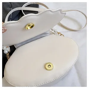 Detail view of the white shell-shaped shoulder bag featuring pearl strap and magnetic clasp.