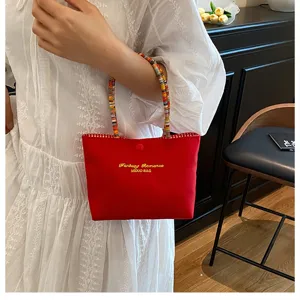 Vue rapprochée du sac à main rouge en tissu avec poignées perlées colorées et texte brodé chic.