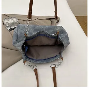 Close-up of casual denim tote bag showing inner zip pocket and stylish chain leather straps.
