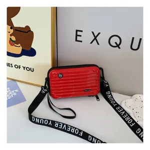 Close-up of red mini hardshell suitcase crossbody bag with ribbed design and letter strap.