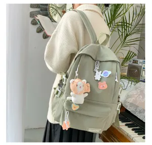Mochila escolar de lona verde claro para estudiantes con lindos colgantes y bolsillos.