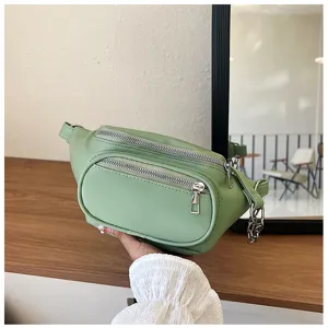 Close-up of light green faux leather fanny pack with multi-zipper compartments and chain detail.