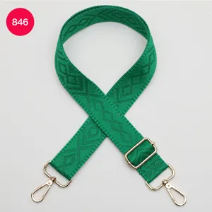 Primo piano dei dettagli della tracolla verde intrecciata con motivo geometrico e ganci dorati.