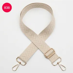Gros plan de la bandoulière de sac tissée beige avec motif chevron et quincaillerie dorée.