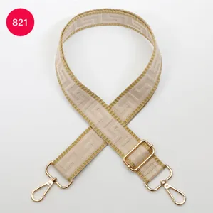 Close-up of beige wide bag strap with geometric pattern, adjustable gold metal hardware.