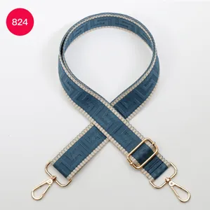 Blue woven wide bag strap with geometric pattern and gold hardware, adjustable crossbody.