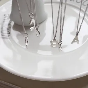 Close-up detail view showing delicate silver letter pendant necklaces on a white plate.