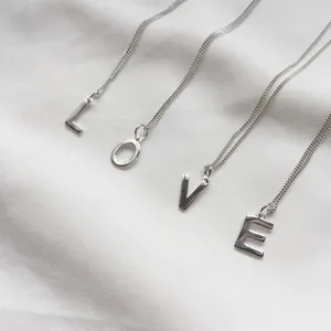 Detailed close-up view of four silver letter pendants spelling LOVE on white fabric.