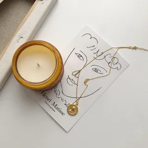 Detailed shot of gold-plated Elizabeth coin pendant necklace styled with candle prop.