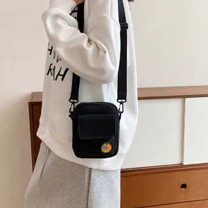Close-up of black canvas crossbody phone bag with front flap pocket and cute fruit patch.