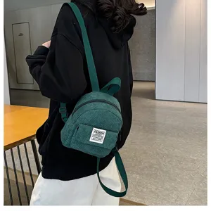 Dark green corduroy mini backpack detail showing soft texture and front pocket design.