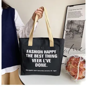 Detailed close-up of a stylish black canvas tote bag featuring contrast straps and a front slogan.