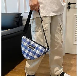 Detail shot of trendy blue and white plaid triangular crossbody bag with black shoulder strap.