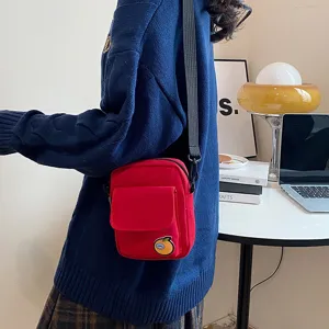 Detail shot of the red canvas crossbody bag featuring a cute orange character patch, worn outdoors.