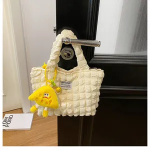 Detalle del bolso de mano beige arrugado con un bonito colgante de felpa de color amarillo.