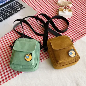 Detailed view of cute canvas crossbody bags in green and brown, featuring a sweet cartoon badge.