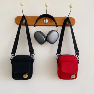 Detailed shot of canvas crossbody phone bags hanging on wooden hook with cute orange patch.