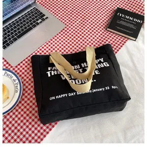 Detail view of a large black canvas tote bag with beige handles and casual slogan prints.