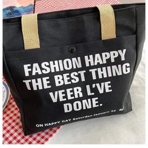 Detail view of black canvas tote bag with white text print, large capacity commuter shoulder bag.
