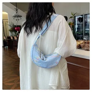 Detailed view of casual light blue shoulder dumpling bag with colorful embroidery and tassel.