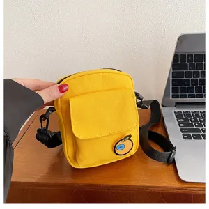 Detailed view of a trendy yellow canvas crossbody bag with a cute orange badge and black strap.
