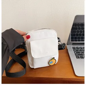 Detailed view of white canvas crossbody bag with cute orange patch and black adjustable strap.