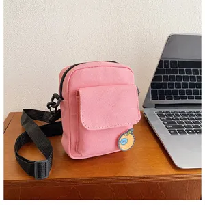 Pink canvas crossbody bag detail shot, featuring cute orange badge and adjustable strap.