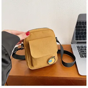 Detail view of small yellow canvas crossbody bag front pocket and cute badge on wooden desk.