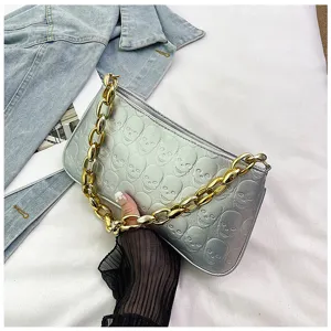 Silver metallic shoulder bag with embossed skulls and chunky gold chain strap for women.