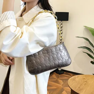 Metallic silver underarm shoulder bag with embossed skull pattern and chunky gold chain strap.
