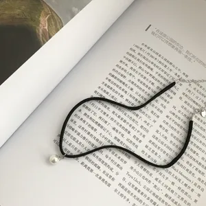 Primo piano di collana choker in velluto nero con ciondolo di perla bianca su libro.