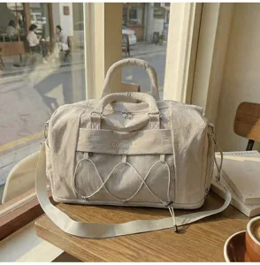 Close-up detail view of the beige travel duffel bag highlighting front mesh pocket and top handles.