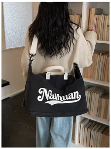 Vista detallada de la bolsa de viaje negra con estampado de letras blancas y correa ajustable.