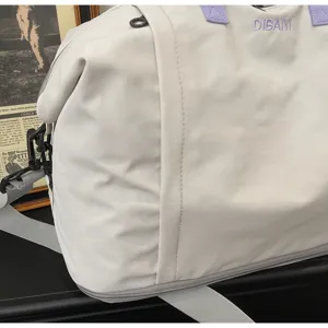 Close-up of white travel duffel bag with purple handles, expandable bottom and grey strap.