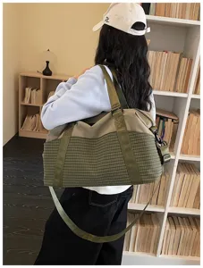 Detailansicht der gruenen karierten Reisetasche getragen von einem Model im Zimmer.