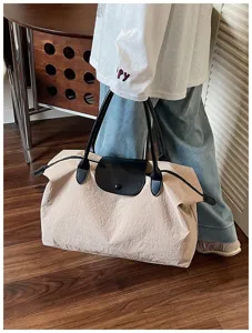 Detailansicht der großen beigen Reisetasche mit schwarzen Ledergriffen und Umschlag.