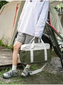 Detail shot of two-tone travel duffel bag with shoulder strap in outdoor camping scene.
