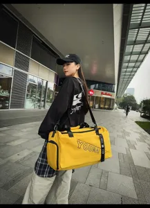 Urban outdoor lifestyle scene showcasing the yellow travel duffel bag side detail worn by model.