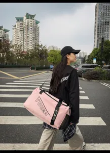 Outdoor detail shot of a large pink travel gym bag with black straps worn by a model in city street.
