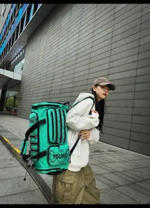 Detailed outdoor shot of the vibrant cyan multi-pocket cylindrical travel duffel backpack.