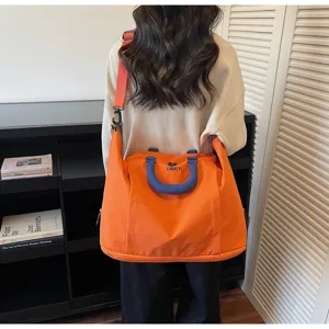 Detailed view of large capacity orange travel bag with shoulder strap and blue handles.