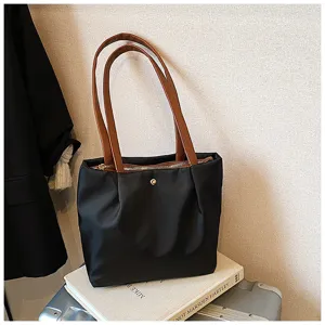 Detailed view of black nylon shoulder tote bag with brown leather handles and gold snap closure.