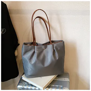 Detailed view of grey nylon tote bag with brown handles, displayed on travel luggage.