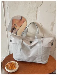 Detail view of large capacity travel duffel bag in light grey, featuring sturdy handles and pockets.